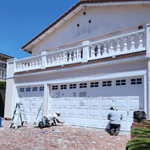 Two GR Repair & Maintenance team members prepping and repainting a residential garage door on a sunny day